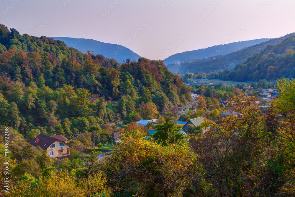 Fototapeta premium Landscape of Plastunka village in the valley and mountains with varicolored trees in sunny autumn day, Sochi, Russia 