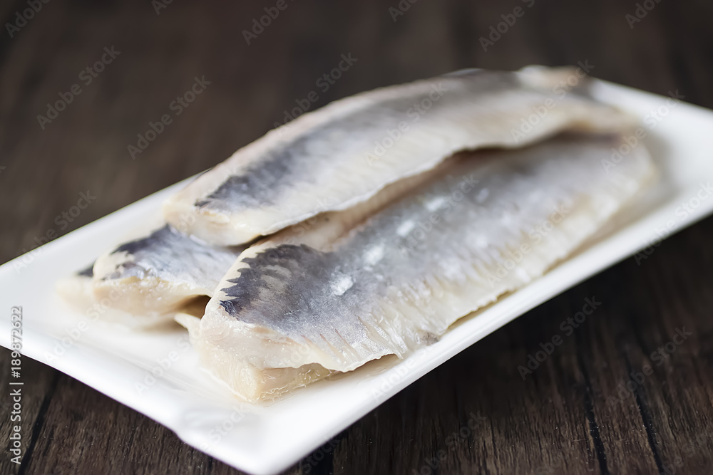 Herring fillets in a white plate on a dark wooden table. Herring fillets in a white plate on a dark wooden table.