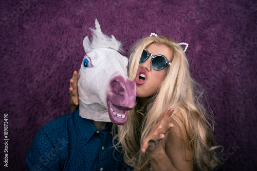 Ταπετσαρία Portrait of happy unicorn in the arms of freaky young woman in sunglasses and kitty ears on the purple background