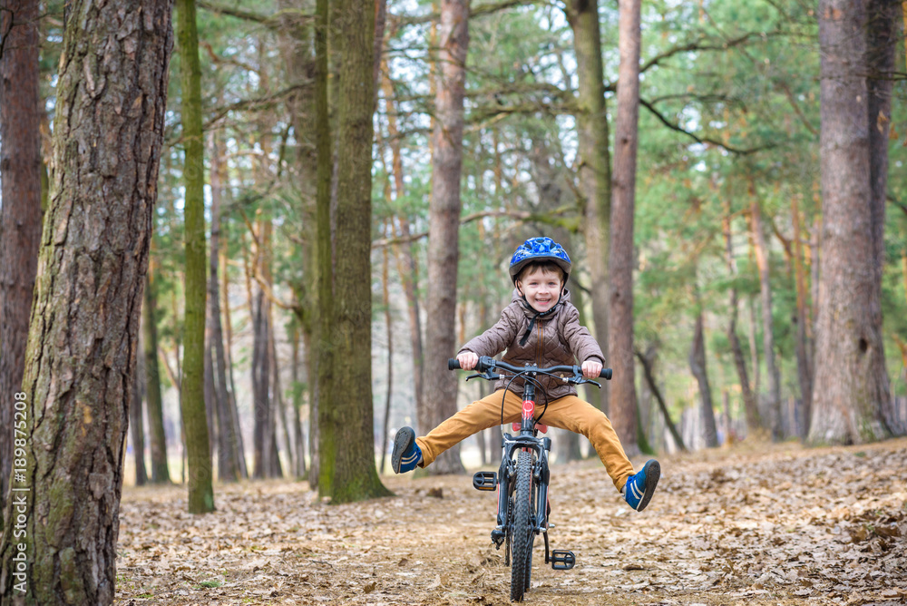 Naklejka premium Happy kid boy of 3 or 5 years having fun in autumn forest with a bicycle on beautiful fall day. Active child wearing bike helmet. Safety, sports, leisure with kids concept.