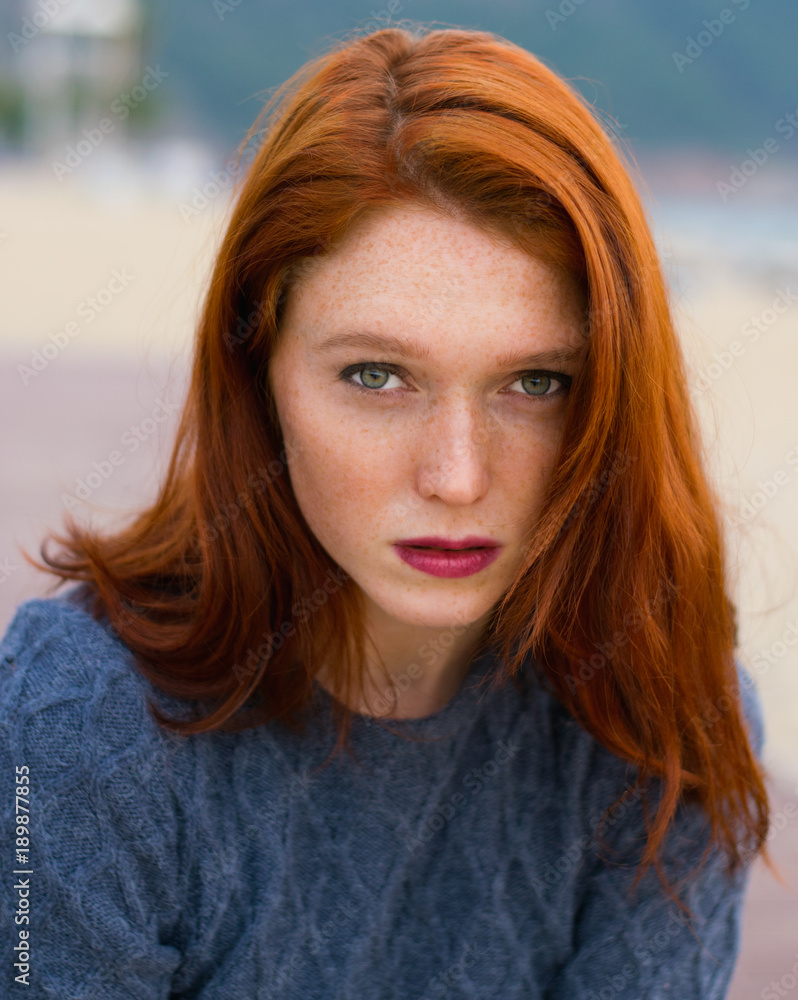 Cute girl with freckles sitting on the beach. Beautiful woman with serious expression. Portrait of a red-haired woman. Lifestyle Vacation Cute girl with freckles sitting on the beach. Beautiful woman with serious expression. Portrait of a red-haired woman. Lifestyle Vacation