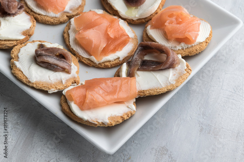 Homemade canapes with smoked salmon, anchovies and cream cheese. Lifht gray background. Copy space.