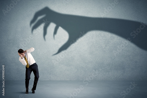 Fotografie Business person afraid of a big monster claw shadow concept