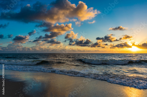 Fototapeta Naklejka Na Ścianę i Meble -  yellow and blue sky reflecting off the wet sand and ocean waters at sunrise