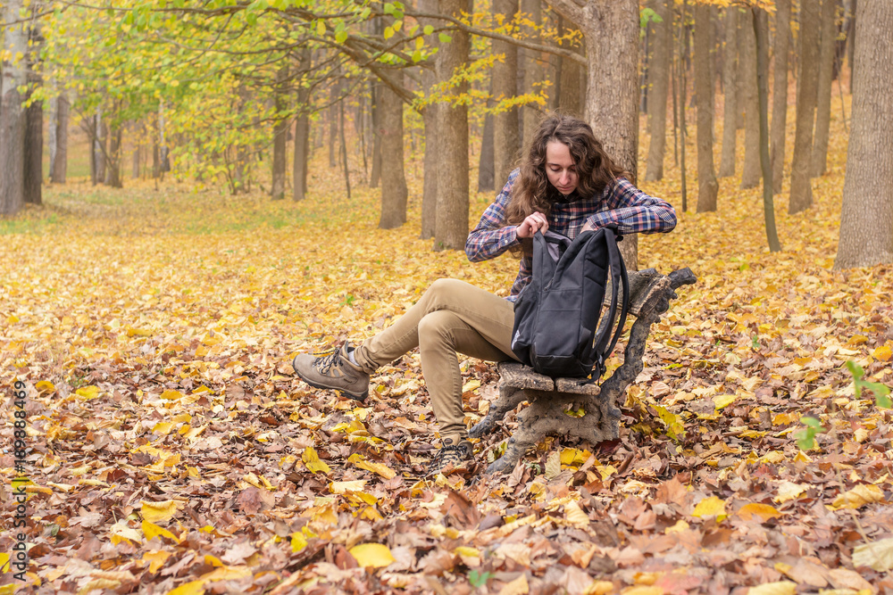 A college girl with long hair trying to find the right things in her bag in the autumn park. A college girl with long hair trying to find the right things in her bag in the autumn park.