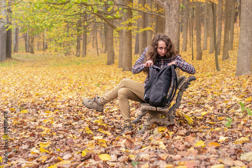 A college girl with long hair trying to find the right things in her bag in the autumn park.