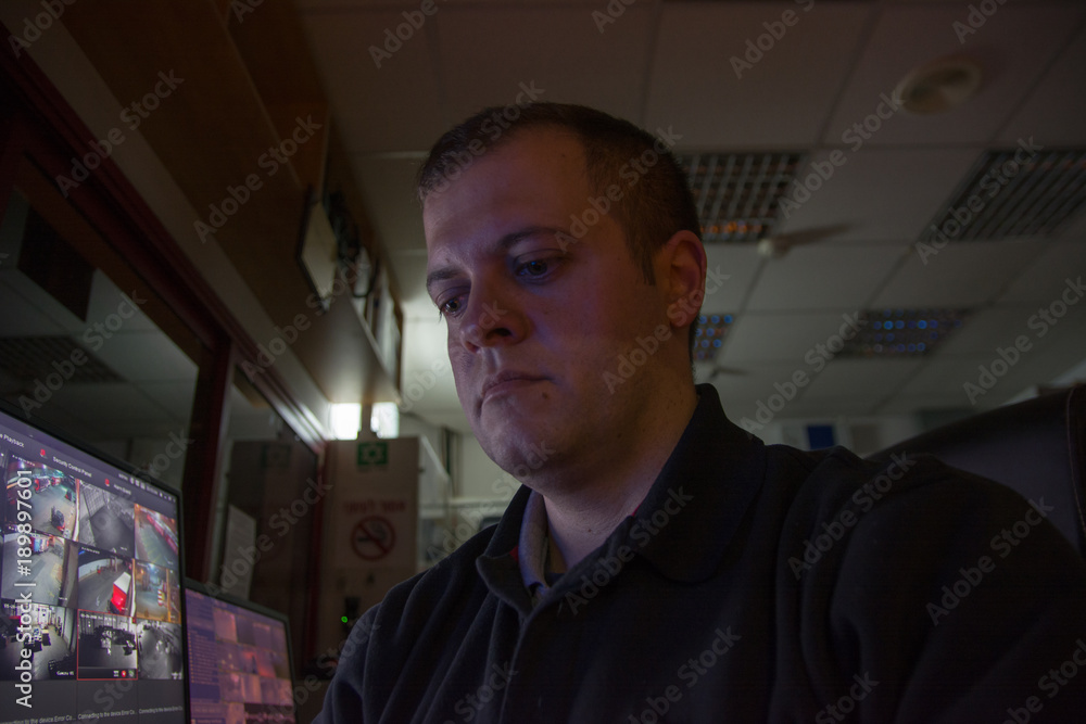 Male security guard on workplace looks at monitor low ligth Male security guard on workplace looks at monitor low ligth