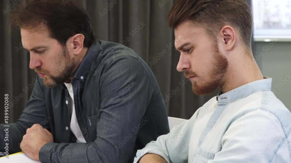 Handsome bearded young man talking to his mature colleague at the office Handsome bearded young man talking to his mature colleague at the office