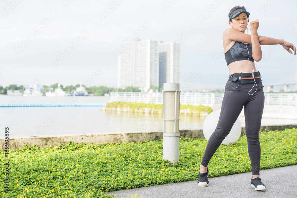 asian woman doing stretching exercises outdoors along city sidewalk