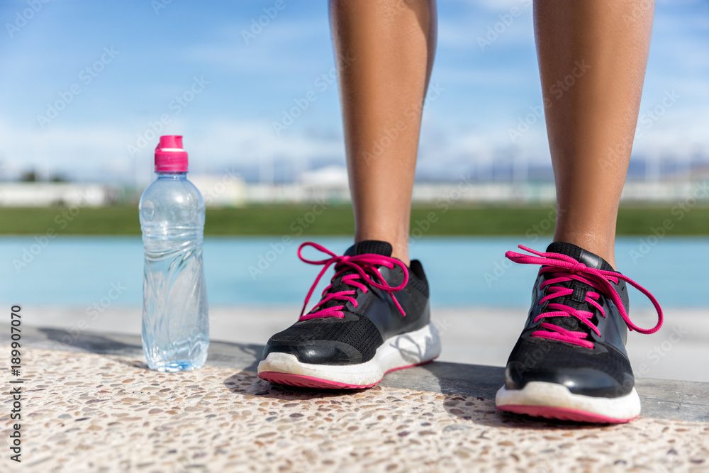 Woman wearing running shoes with water bottle ready to go jogging oon running tracks in stadium. Pink laces footwear.
