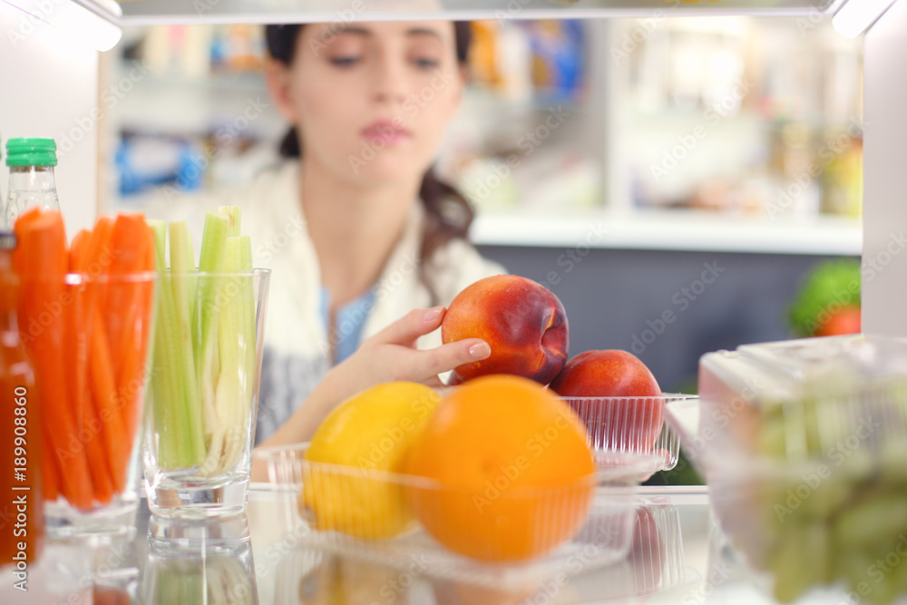 Portrait of female standing near open fridge full of healthy food, vegetables and fruits. Portrait of female Portrait of female standing near open fridge full of healthy food, vegetables and fruits. Portrait of female