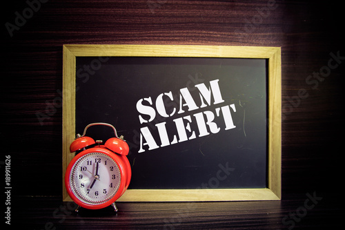 SCAM ALERT text written on blackboard with red clock .