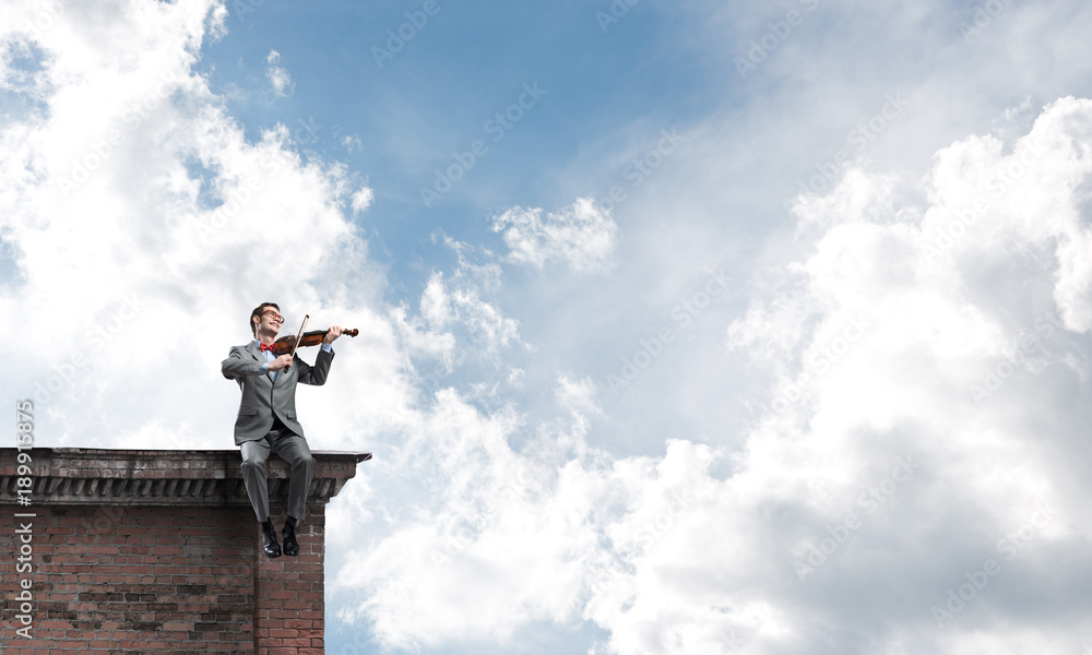 Handsome violinist in glasses on building edge play his melody