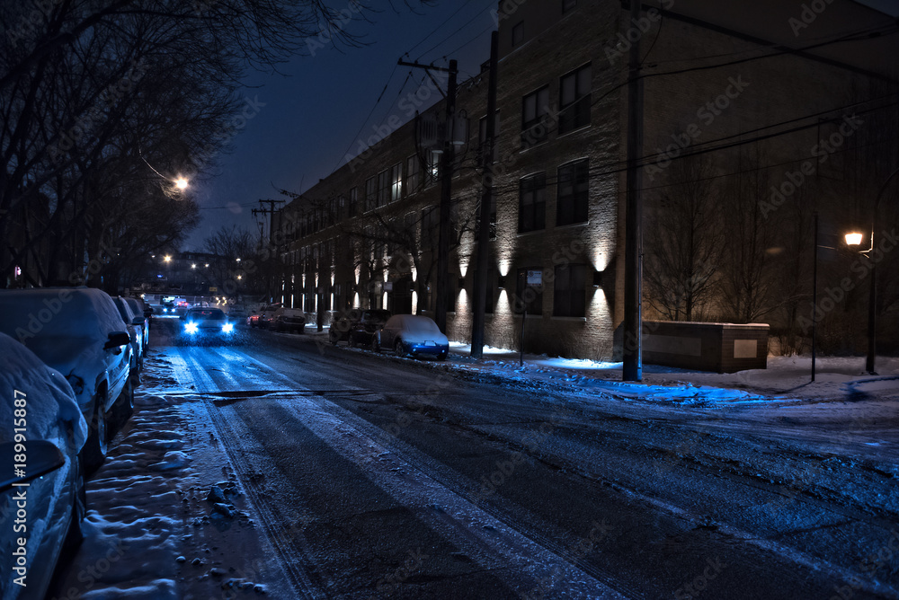Dark and cold Chicago winter street with snow and ice and an oncoming car at night.