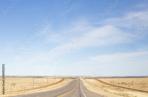 A long stretch of road in a dry climent with a beautiful blue sky