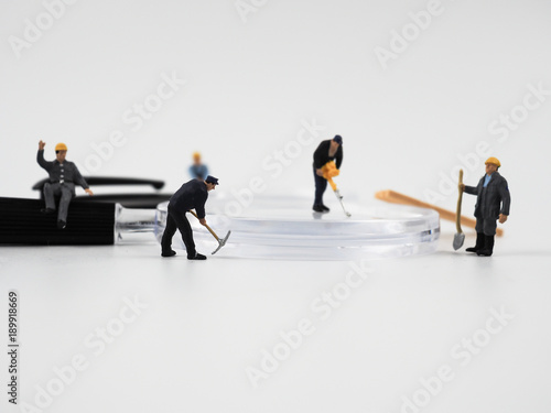 Miniature construction worker is working on a magnifying glass on a white background.