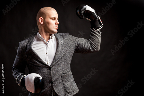 A young man busenessman in a white shirt, gray suit, boxing gloves posing and show biceps on a black isolated background photo