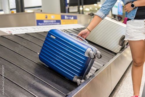 Suitcase on luggage conveyor belt at baggage claim at airport. Lines of people waiting for their baggage