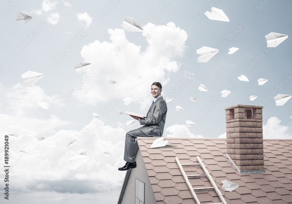 Man on brick roof reading book and paper planes flying in air Man on brick roof reading book and paper planes flying in air