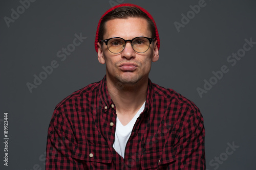 Portrait of young stylish thoughtful hipster guy looking at the camera on gray background © pavel_shishkin