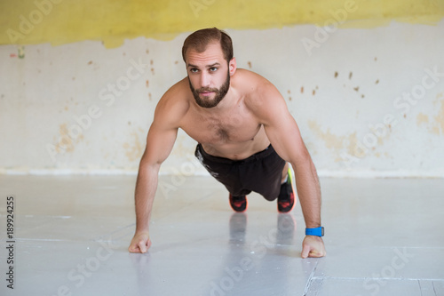 Strength and motivation. Side view of young handsome man in sportswear doing push-up at gym