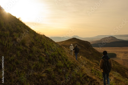 Three hikers on mountain ridge, golden sunrise