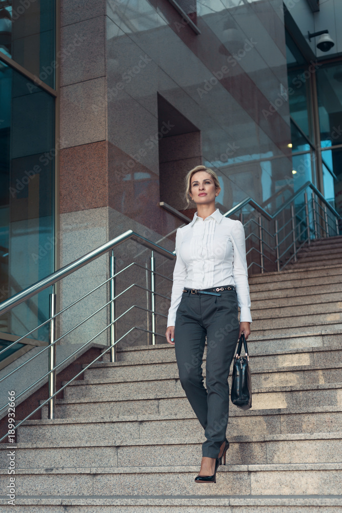 Business woman in pants with briefcase walking on stairs