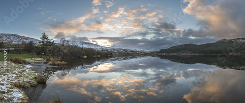 Stunning sunrise landscape image in Winter of Llyn Cwellyn in Snowdonia National Park with snow capped mountains in background