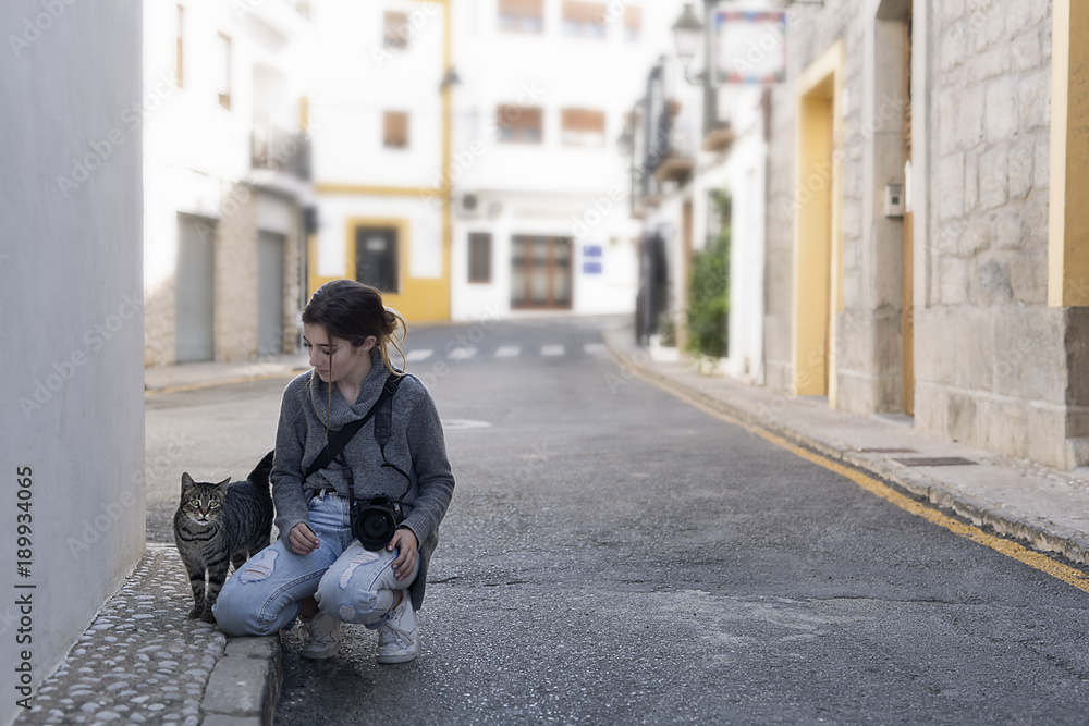 Teenage girl with her photo camera greeting a street cat.