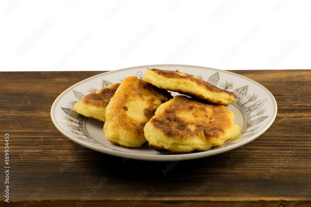 Syrniki on a white plate on a wooden board. Cheese pancakes. Breakfast.