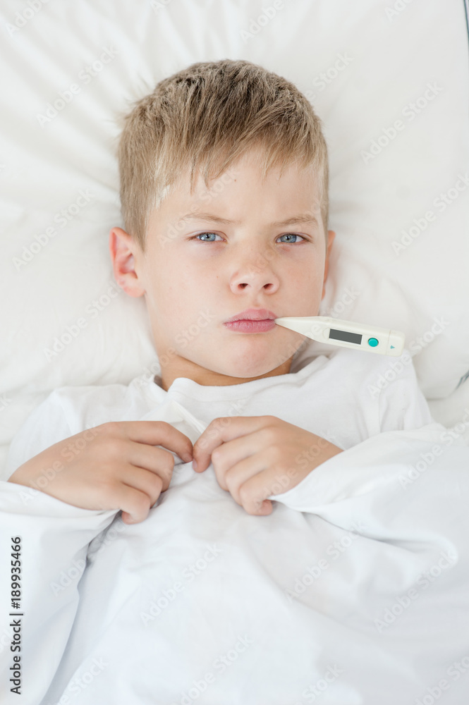 Sick boy with thermometer in mouth lying on the bed Sick boy with thermometer in mouth lying on the bed