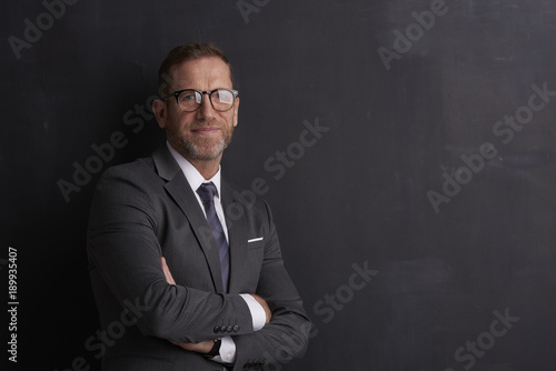 Confident middle aged businessman.Portrait shot of a smiling middle aged businessman looking at camera while standing at dark background. 