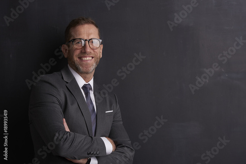 Confident middle aged businessman.Portrait shot of a middle aged businessman with toothy smile looking at camera while standing at dark background. 