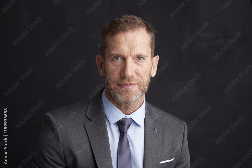 Confident middle aged businessman.Portrait shot of a middle aged businessman with toothy smile looking at camera while standing at dark background. Confident middle aged businessman.Portrait shot of a middle aged businessman with toothy smile looking at camera while standing at dark background.