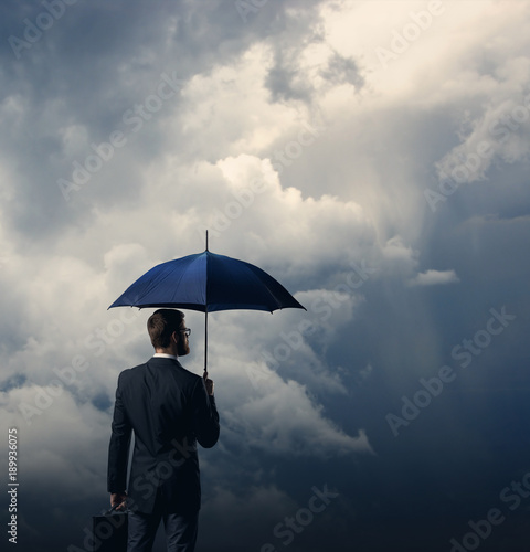 Businessman with umbrella standing over stormy background.