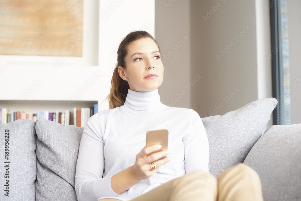 Online and mobile banking. A smiling brunette mature woman relaxing on her couch and text messaging on her cell phone. Online and mobile banking. A smiling brunette mature woman relaxing on her couch and text messaging on her cell phone.