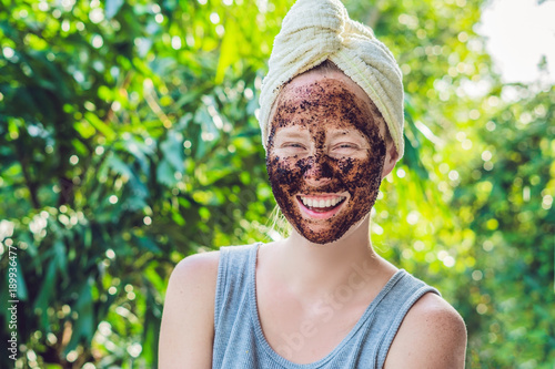 Face Skin Scrub. Portrait Of Sexy Smiling Female Model Applying Natural Coffee Mask, Face Scrub On Facial Skin. Closeup Of Beautiful Happy Woman With Face Covered With Beauty Product. High Resolution photo