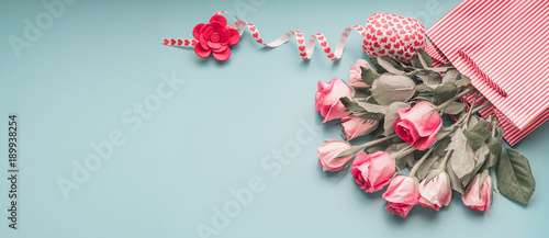 Fototapeta Naklejka Na Ścianę i Meble -  Greeting pink pale roses bunch in shopping bag with ribbon on turquoise blue background, top view, copy space. Female holidays banner or template layout.