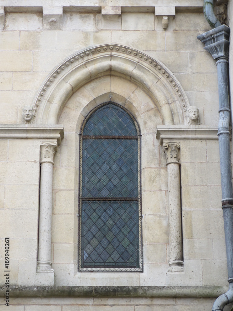 Visages sculptés de part et d'autre d'un vitrail d'une église