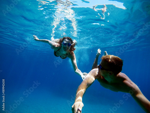Underwater selfie with a stick of young excited happy love student couple swimming and enjoying with goggles in the exotic turquoise sea at summer vacation.