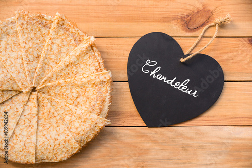 Top view of crepes (french pancakes), word chandeleur (meaning candlemas) written on a heart, rustic wood background