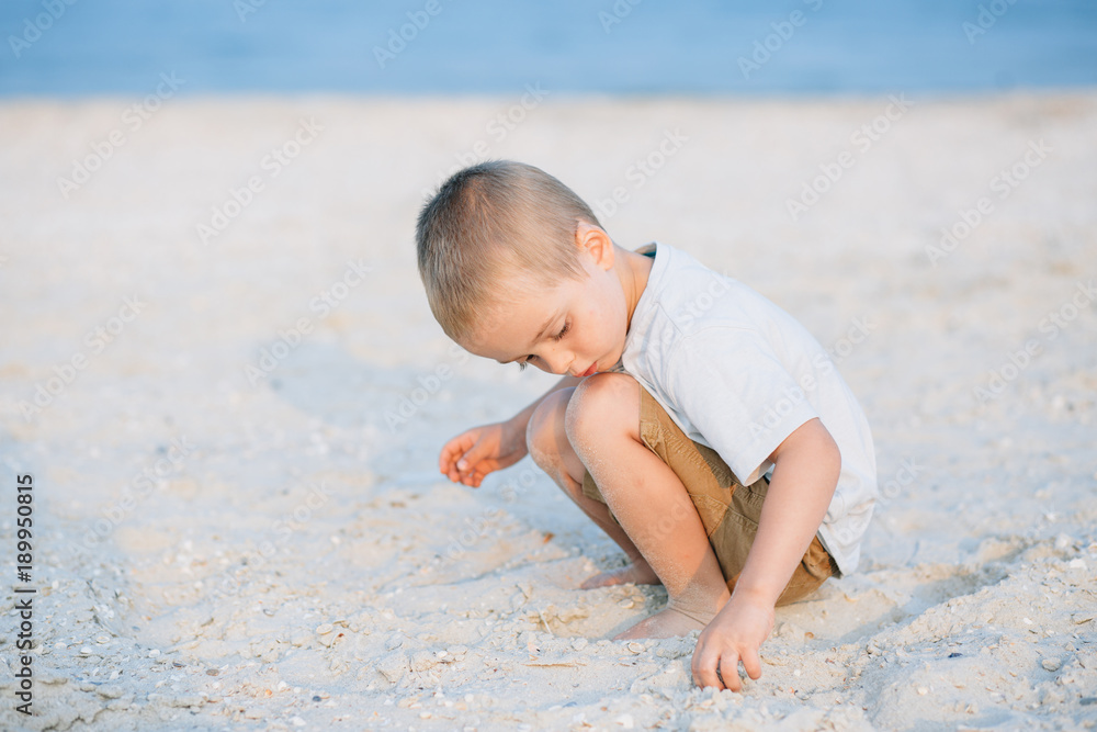 Portrait serious little boy playing in the sand near the sea, ocean. Positive human emotions, feelings, joy. Funny cute child taking vacations and enjoying summer. Portrait serious little boy playing in the sand near the sea, ocean. Positive human emotions, feelings, joy. Funny cute child taking vacations and enjoying summer.