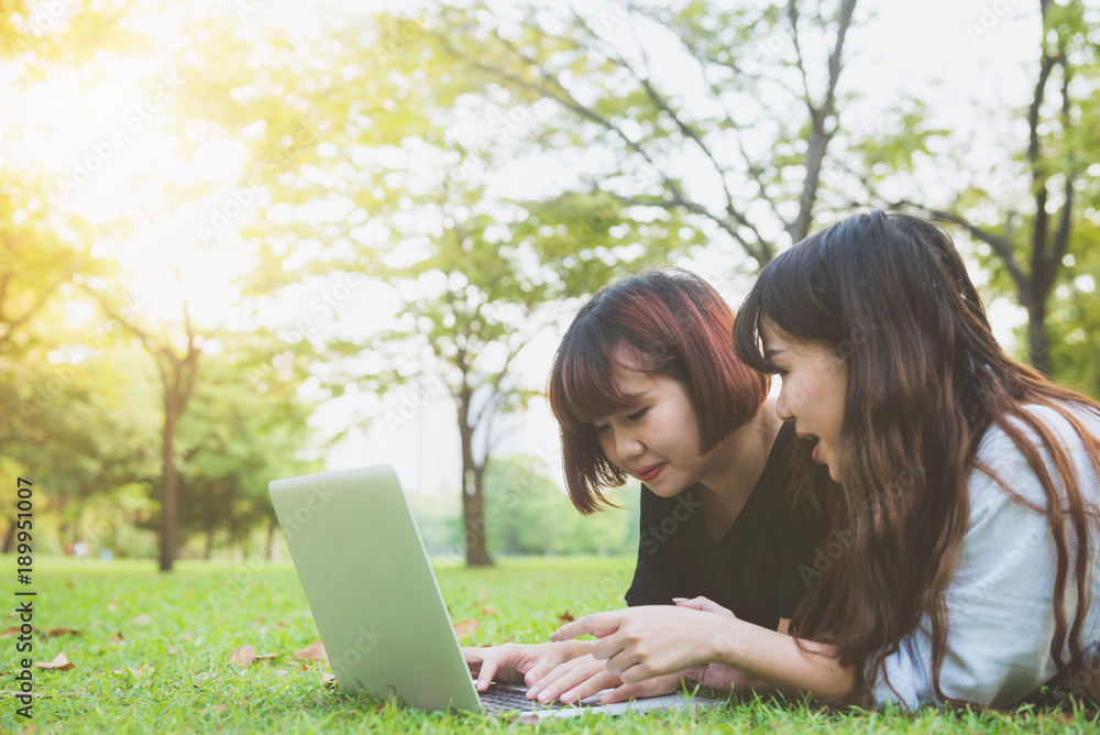 Young asian women lying on grass and using laptop and typing. Girls hands on keyboard. Distance learning concept. Happy hipster young asian women working on laptop in park. Student studying outdoors. Young asian women lying on grass and using laptop and typing. Girls hands on keyboard. Distance learning concept. Happy hipster young asian women working on laptop in park. Student studying outdoors.