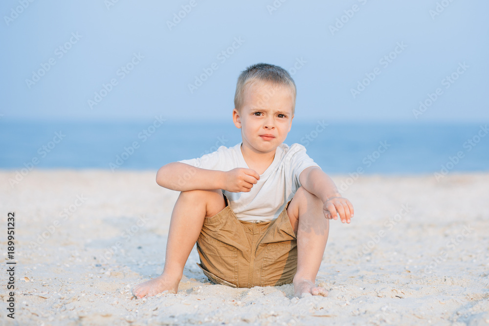 Serious cute little boy near water at the beach on hot summer day. Having fun during vacation. Serious cute little boy near water at the beach on hot summer day. Having fun during vacation.