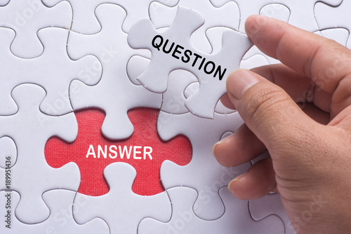 Hand holding piece of jigsaw puzzle with word question & answer.