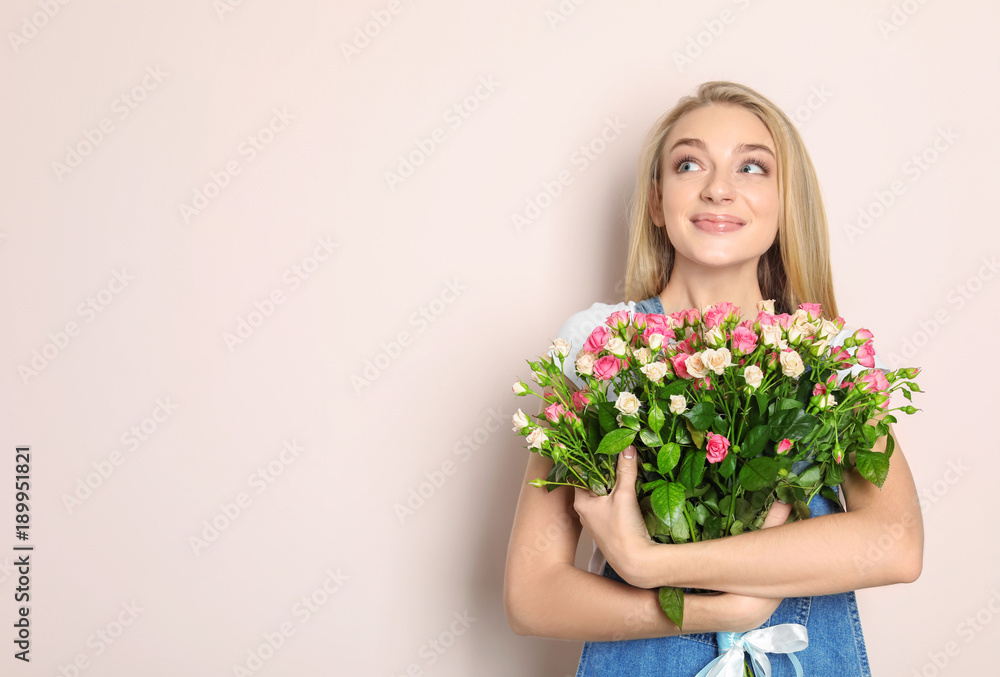 Beautiful young woman with bouquet of roses on color background