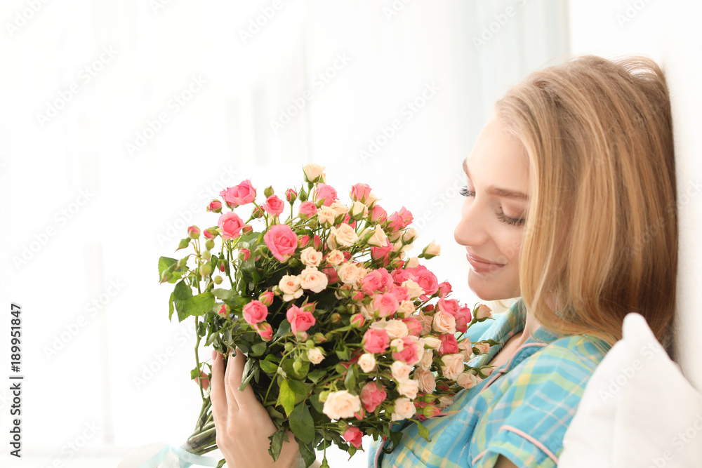 Beautiful young woman with bouquet of roses at home