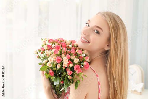 Beautiful young woman with bouquet of roses at home