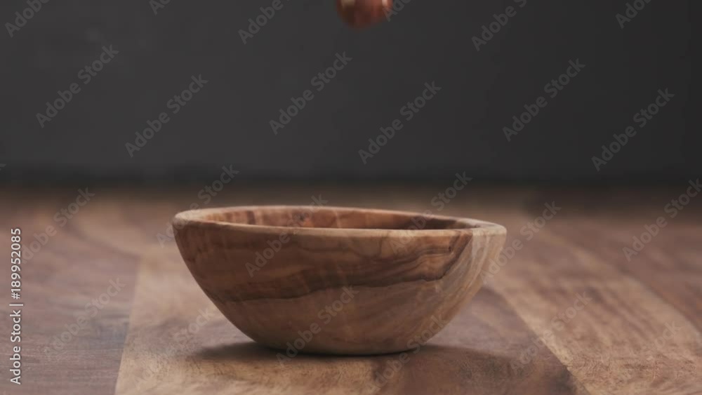 Slow motion roasted hazelnuts falling into wood bowl Slow motion roasted hazelnuts falling into wood bowl