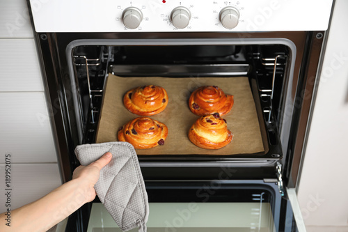 Woman taking baking sheet with buns from oven, closeup